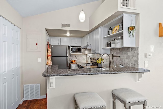 kitchen featuring stainless steel appliances, dark stone countertops, under cabinet range hood, backsplash, and lofted ceiling