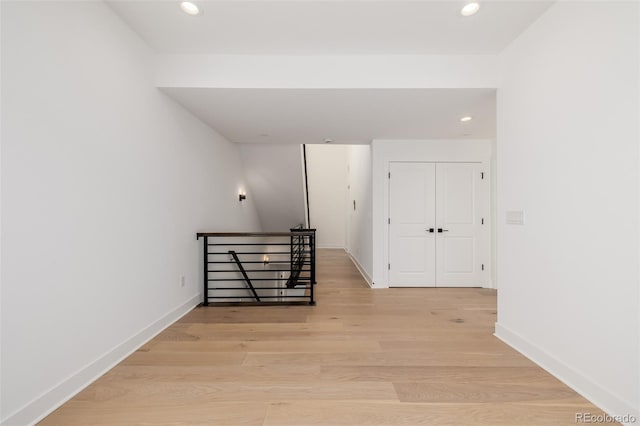 hall with light wood-style floors, baseboards, an upstairs landing, and recessed lighting