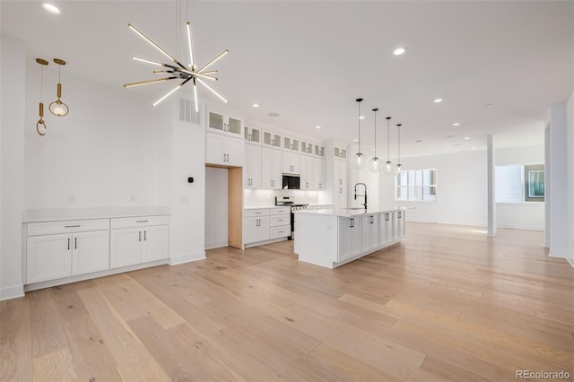 kitchen with glass insert cabinets, white cabinets, appliances with stainless steel finishes, a sink, and light wood finished floors