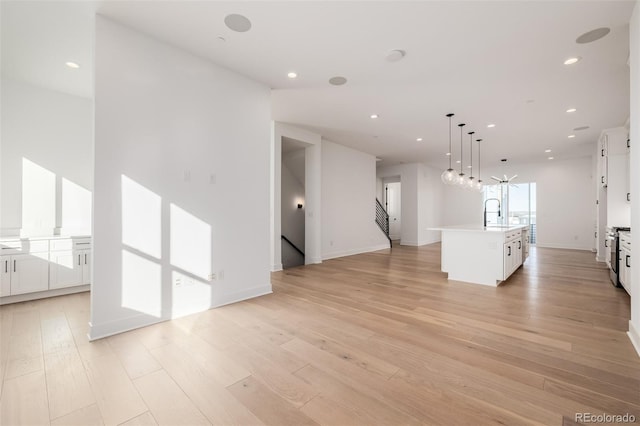 unfurnished living room with a sink, light wood-style flooring, recessed lighting, and stairway