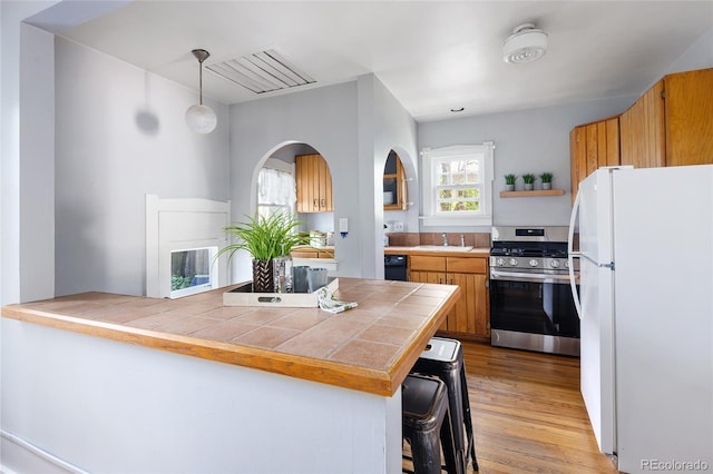 1838 S Williams St, Denver, CO 80210 - kitchen with freestanding refrigerator, stainless steel gas stove, tile counters, open shelves, and light wood-style floors
