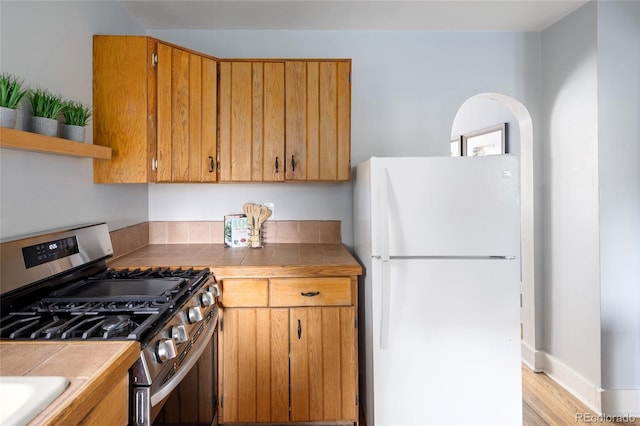 1838 S Williams St, Denver, CO 80210 - kitchen featuring freestanding refrigerator, stainless steel gas range oven, tile countertops, light wood-style floors, and open shelves