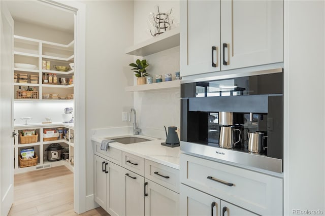 interior space featuring white cabinets, sink, light wood-type flooring, and light stone counters