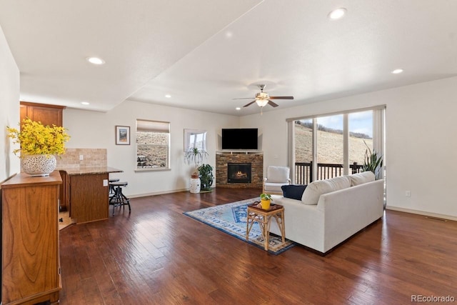 living area featuring baseboards, a stone fireplace, dark wood-style flooring, and recessed lighting