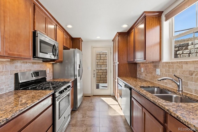 kitchen featuring stainless steel appliances, brown cabinetry, a sink, and stone counters