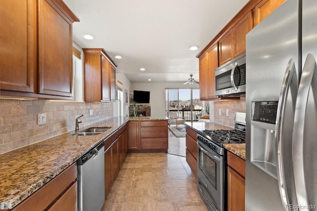 kitchen featuring backsplash, appliances with stainless steel finishes, brown cabinetry, a sink, and dark stone countertops