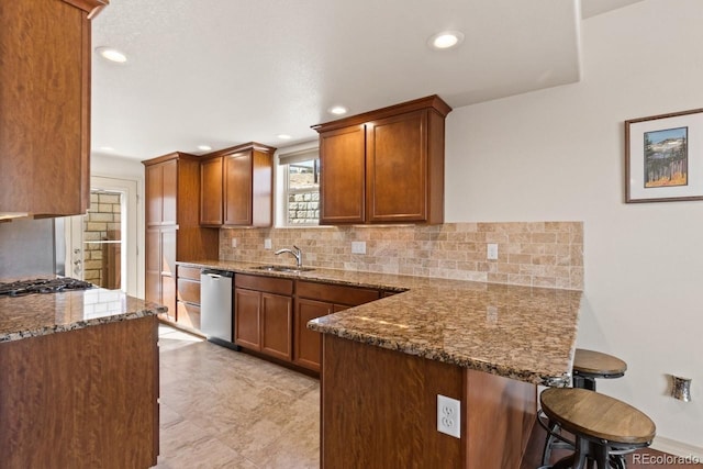 kitchen with decorative backsplash, dark stone counters, appliances with stainless steel finishes, a breakfast bar area, and a peninsula