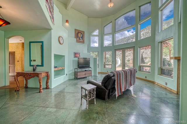 living room featuring a towering ceiling, beamed ceiling, and concrete flooring