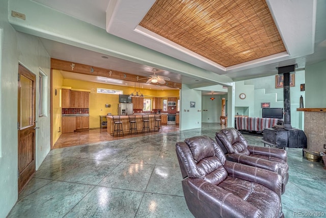 living room with a raised ceiling, a wood stove, and ceiling fan