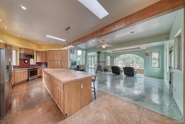 kitchen with appliances with stainless steel finishes, a skylight, a kitchen island, and ceiling fan