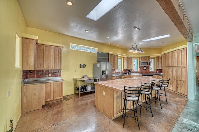 kitchen featuring a skylight, a kitchen bar, stainless steel appliances, backsplash, and a kitchen island