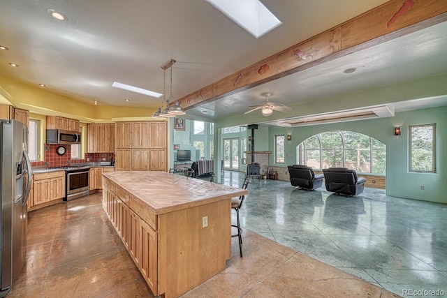 kitchen featuring a kitchen breakfast bar, a center island, stainless steel appliances, a skylight, and ceiling fan