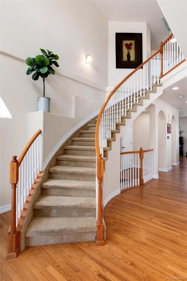 stairway with arched walkways, a high ceiling, baseboards, and wood finished floors