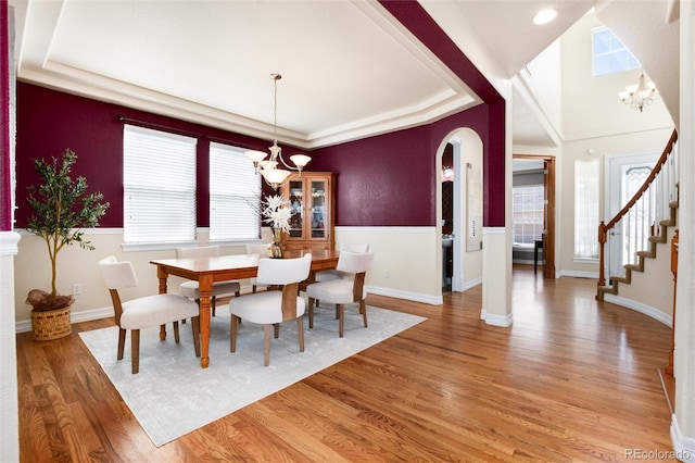 dining area with arched walkways, visible vents, a chandelier, wood finished floors, and stairs