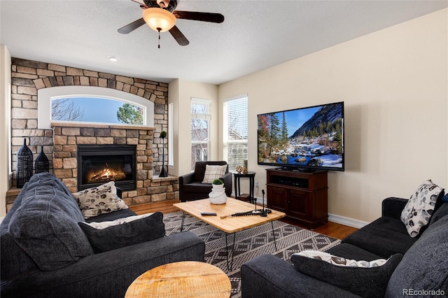 living area featuring a fireplace, ceiling fan, baseboards, and wood finished floors