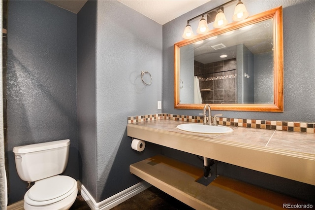 bathroom with visible vents, baseboards, toilet, a textured wall, and vanity