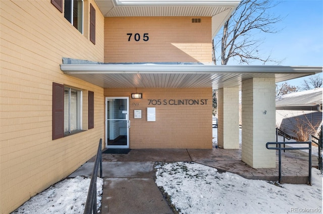 snow covered property entrance featuring brick siding