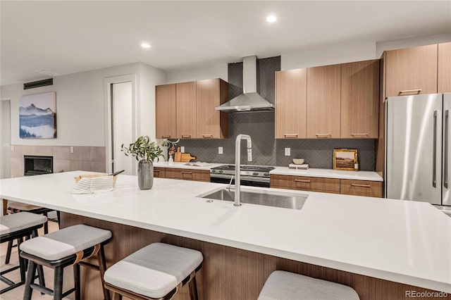 kitchen with decorative backsplash, sink, wall chimney range hood, stainless steel refrigerator, and a breakfast bar area