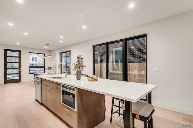 kitchen with light brown cabinetry, a kitchen island with sink, sink, and light hardwood / wood-style flooring