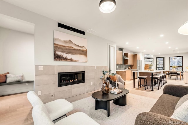 living room featuring light wood-type flooring and a tiled fireplace