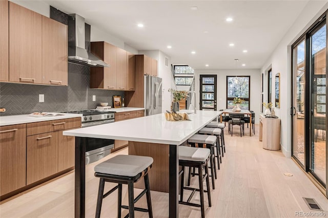 kitchen featuring a center island, wall chimney exhaust hood, stainless steel appliances, light hardwood / wood-style floors, and a breakfast bar area