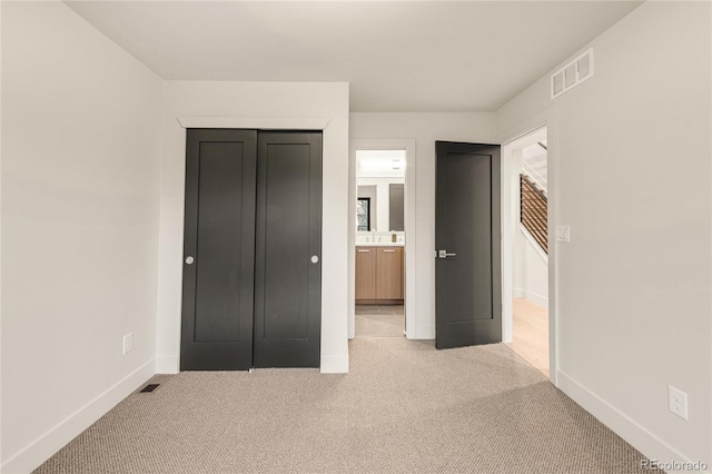 unfurnished bedroom featuring light carpet, a closet, and ensuite bathroom