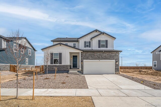 view of front of property with stone siding, fence, a garage, board and batten siding, and driveway