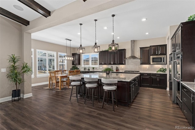 kitchen with a kitchen island, pendant lighting, stainless steel appliances, dark brown cabinets, and wall chimney exhaust hood