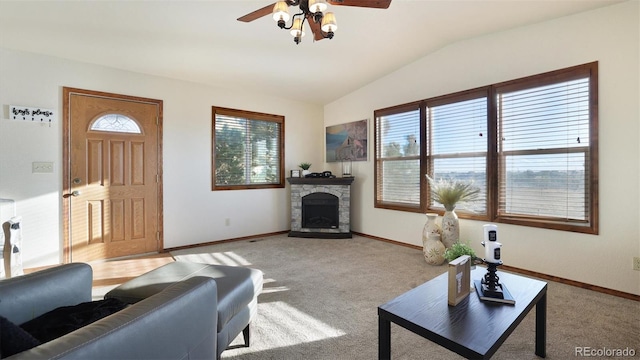 living room featuring light carpet, a stone fireplace, vaulted ceiling, and ceiling fan