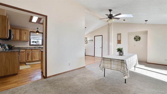 interior space with vaulted ceiling with skylight, sink, ceiling fan, light carpet, and a textured ceiling