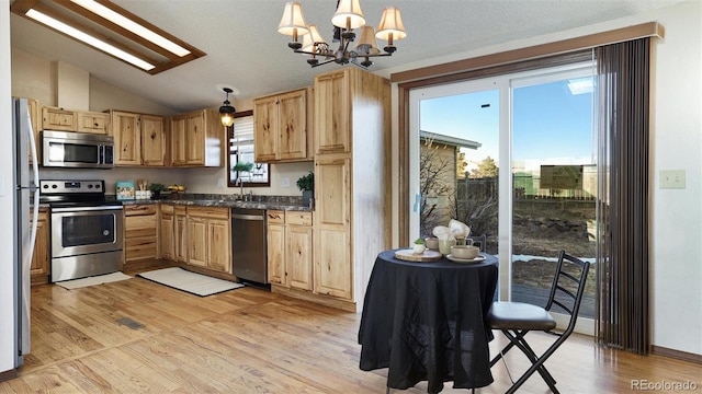 kitchen featuring pendant lighting, lofted ceiling, appliances with stainless steel finishes, a chandelier, and light wood-type flooring