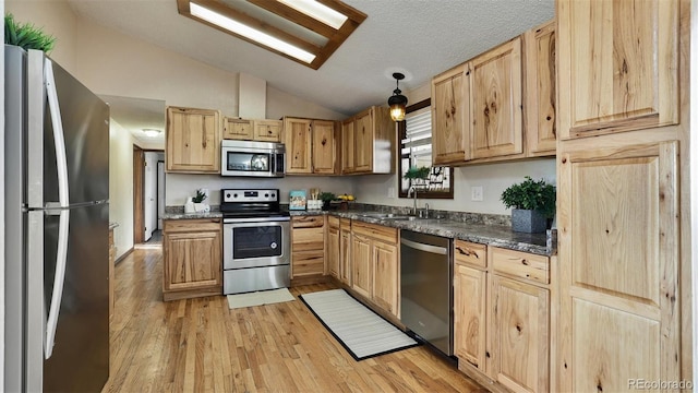 kitchen with sink, light hardwood / wood-style flooring, appliances with stainless steel finishes, hanging light fixtures, and vaulted ceiling