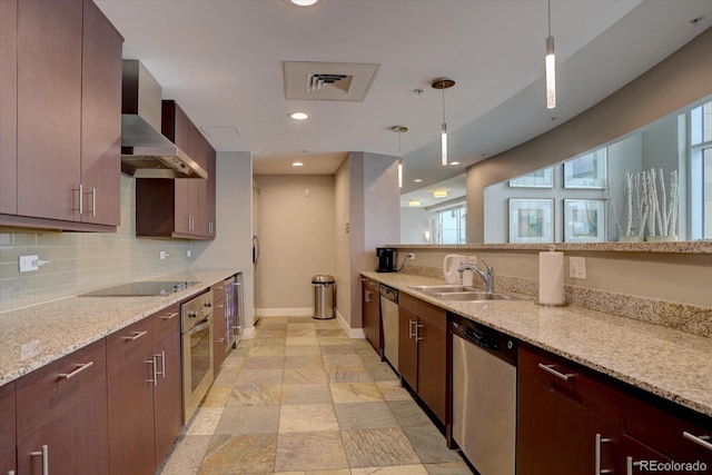 kitchen featuring pendant lighting, wall chimney range hood, sink, light stone counters, and stainless steel appliances