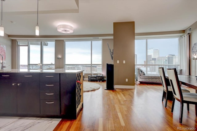 kitchen with pendant lighting, dark brown cabinets, light hardwood / wood-style floors, and light stone countertops