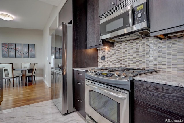 kitchen featuring dark brown cabinets, light stone countertops, stainless steel appliances, and tasteful backsplash