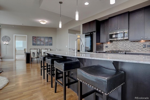 kitchen with backsplash, a kitchen breakfast bar, hanging light fixtures, light stone countertops, and light hardwood / wood-style floors