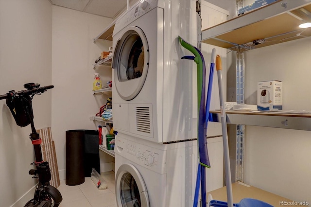 laundry area with stacked washer / drying machine and light tile patterned floors