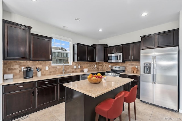 kitchen featuring sink, a kitchen island, a breakfast bar, backsplash, and appliances with stainless steel finishes