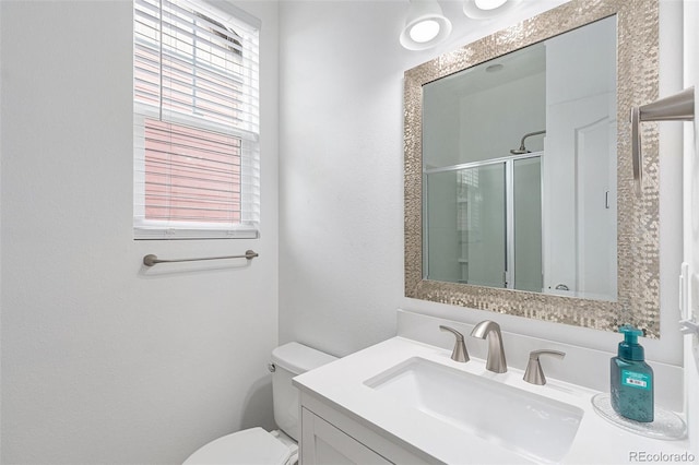 bathroom with toilet, vanity, a shower with door, and a healthy amount of sunlight