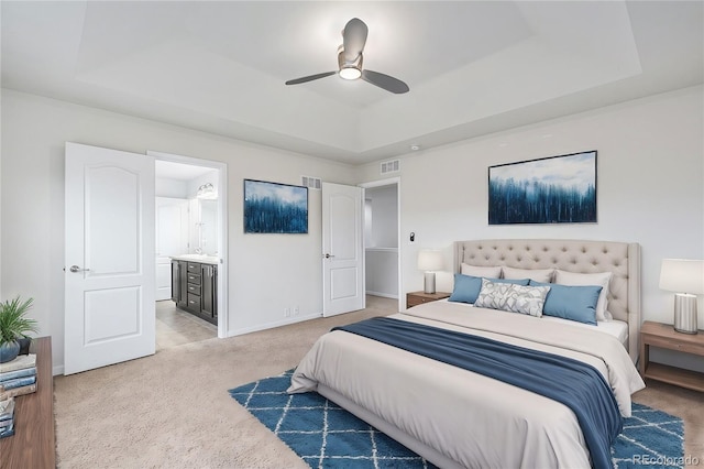 bedroom featuring light carpet, sink, ceiling fan, a tray ceiling, and connected bathroom