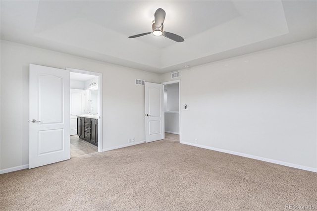 unfurnished bedroom with ensuite bathroom, ceiling fan, light carpet, and a tray ceiling