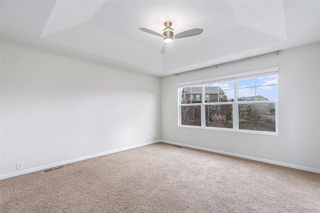 carpeted empty room featuring ceiling fan and a raised ceiling