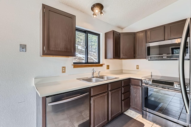 kitchen featuring a sink, stainless steel appliances, vaulted ceiling, dark brown cabinetry, and a textured ceiling