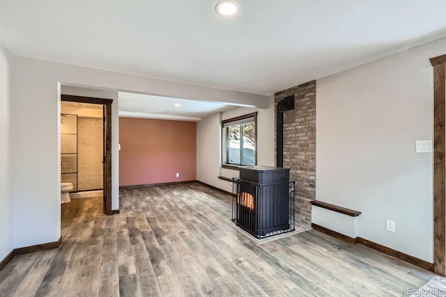 unfurnished living room with a wood stove, wood finished floors, and baseboards