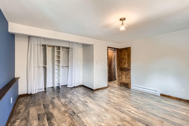 unfurnished bedroom with a closet, baseboard heating, baseboards, and wood finished floors