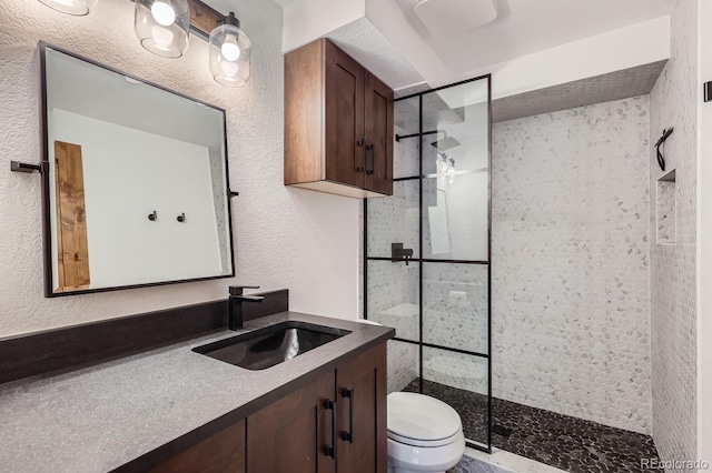 bathroom with a textured wall, toilet, vanity, and a walk in shower