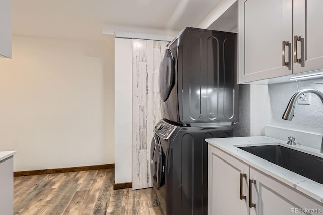 clothes washing area with baseboards, light wood-type flooring, stacked washer and dryer, cabinet space, and a sink