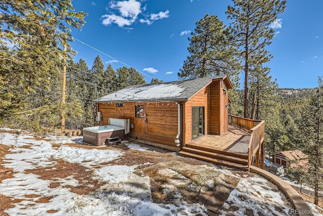 view of snow covered exterior with a deck, a shingled roof, and a hot tub