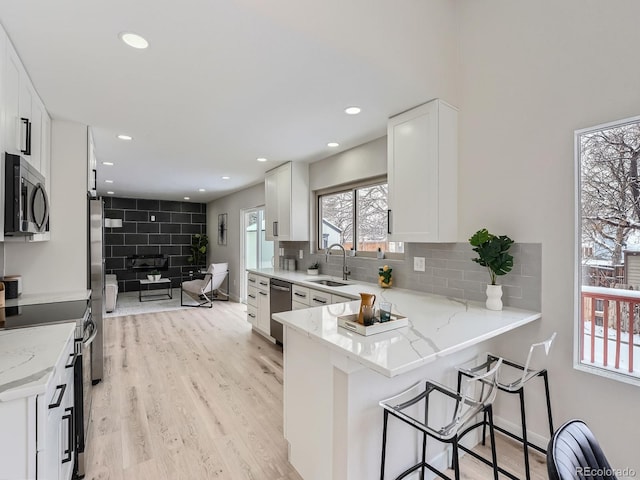 kitchen with white cabinetry, light stone countertops, kitchen peninsula, and stainless steel appliances