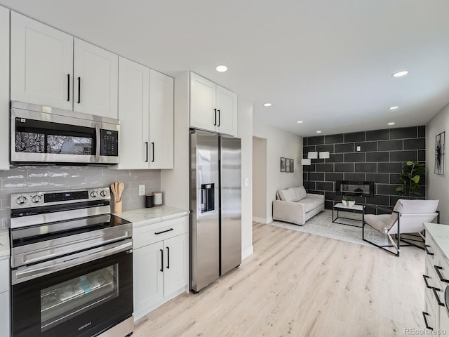 kitchen featuring backsplash, white cabinets, light wood-type flooring, light stone countertops, and stainless steel appliances